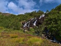 Waterfall near SÃÂ¸rvÃÂ¥gen, MoskenesÃÂ¸y, Lofoten, Norway on summer day surrounded by colorful meadow and trees.