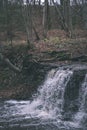 waterfall over the rocks in river stream in forest in late autumn with naked trees and grey colors in nature - vintage old film Royalty Free Stock Photo