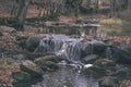 waterfall over the rocks in river stream in forest in late autumn with naked trees and grey colors in nature - vintage old film Royalty Free Stock Photo