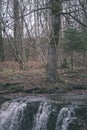 waterfall over the rocks in river stream in forest in late autumn with naked trees and grey colors in nature - vintage old film Royalty Free Stock Photo