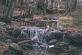 waterfall over the rocks in river stream in forest in late autumn with naked trees and grey colors in nature - vintage old film Royalty Free Stock Photo