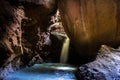 Waterfall of a small stream of fresh water coming out entering a dark cavern rocky brown colors and green moss