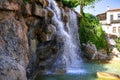 Waterfall from a stone cliff close-up. Falling and splashing streams of water against the background of a modern building on a Royalty Free Stock Photo