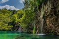 Waterfalls coming down from tall cliffs to turquoise coloured lake in Plitvice Lakes