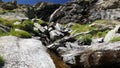Waterfalls flowing in idyllic uncontaminated environment crossing green meadows and boulders on the Alps in summer.