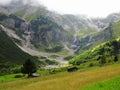 High mountain waterfall rivulets into green valley with huts in alpine terrain Royalty Free Stock Photo