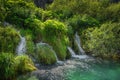 Waterfalls surrounded by tall grass flowing in to turquoise coloured lake, Plitvice Lakes