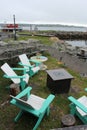 A waterfront scene with white and turquoise chairs next to old lobster traps with the ocean and an old boat in the background. Royalty Free Stock Photo