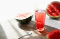 Watermelon juice smoothies in a high transparent glass, half and slices of watermelon in the background in hard Sunny shadows