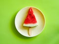 Watermelon slice on a ice cream stick on yelow plate isolated on green background.