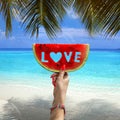 Watermelon slice with text love, woman hands holding it against blue sky and Indian ocean. Summertime concept.Tropical island Royalty Free Stock Photo