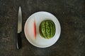 A watermelon on a white plate with a knife Royalty Free Stock Photo