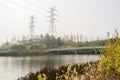 Waterside grass,fenced footbridge and electricity pylons in sunny winter afternoon