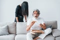 Wathing TV with scary woman with black hair near him. Senior stylish modern man with grey hair and beard indoors