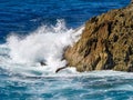 Wave action onto rocky outcrop. Blue seas, white wave orange rock Royalty Free Stock Photo