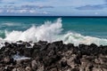 Wave breaking on black lava rock in Hawaii.White spray in the air. Ocean, blue sky and clouds in background. Royalty Free Stock Photo