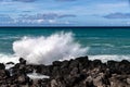 Wave breaking on black lava rock in Hawaii.White spray in the air. Ocean, blue sky and clouds in background. Royalty Free Stock Photo