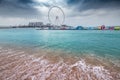 wave crashes on the sandy beach and the famous Dubai Eye Ferris Wheel during cloudy weather