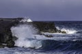 Wave crashing on volcanic rocks, black sand beach in hawaii. Ocean, blue sky in background. Royalty Free Stock Photo