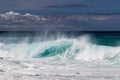 Wave breaking on western Kona coast in Hawaii. White spray and foam on the water. Rocks in foreground.