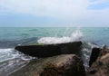 The wave is lapping over a square rock on the pier covered in green algae. The emerald-colored sea splashes against the concrete