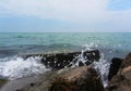 The wave is lapping over a square rock on the pier covered in green algae. The emerald-colored sea splashes against the concrete