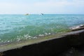 The wave is lapping over a square rock on the pier covered in green algae. The emerald-colored sea splashes against the concrete