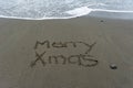 Merry Xmas hand written in the sand with the sea in the background