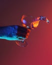 Wave. Male hand pouring clean fluid from cocktail glass over bright dark red background in neon light. Art, drinks Royalty Free Stock Photo