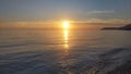 A wave rolls onto the sea pebble beach. The sun sinks behind the sea horizon and colors the sky and clouds in delicate tones. Coas Royalty Free Stock Photo