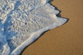 Wave of the sea entering the sand of the beach forming foam, contrast of white and beige. Macro photography Royalty Free Stock Photo