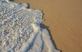 Wave of the sea entering the sand of the beach forming foam, contrast of white and beige. Macro photography Royalty Free Stock Photo