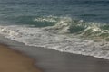 Wave swell rising up at edge of washback foam, with bacspray, on snady shore