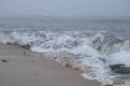 Waves breaking on shore of foggy beach with mist on ocean early in the morning