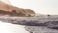 Waves breaking on the shore of a Tenerife beach with back light of the oncoming sunset