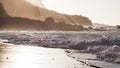 Waves breaking on the shore of a Tenerife beach with back light of the oncoming sunset