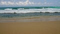 Waves crash onto sandy beach in clear weather. Warm sand meets turquoise sea with frothy whitecaps. Uninhabited