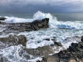 waves crash on a rocky shore with cloudy sky above it