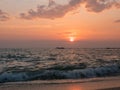 Waves crash on sandy beach at sunset with vivid orange sky