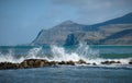 Waves crash on sea defense with a hilly peninsula in North Wales