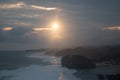 Waves crashing against rocks and sand beach at sunset with sunbeam and cloud sky