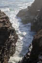 waves crashing against a rocky shoreline under the soft glow of sunlight, casting mist and foam