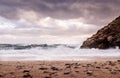 Waves crashing on a deserted, dramatic beach with dark moody clouds in the sky Royalty Free Stock Photo