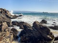 Waves crashing on rocky coast with cargo ships by Valparaiso port