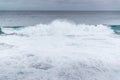 Waves crashing into a rocky shore full of large rocks and breaking water leaping to the sides with a pair of boats moored on the