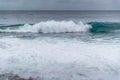 Waves crashing into a rocky shore full of large rocks and breaking water leaping to the sides with a pair of boats moored on the