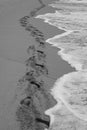 Waves follow the track of human footprints on a beach`s sand