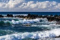 Waves on Hawiian shore; volcanic rocks in surf. Pacific in distance, with blue sky and clouds. Royalty Free Stock Photo