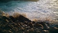Waves hitting beach rocks in morning sunlight. Closeup foaming water splashing Royalty Free Stock Photo