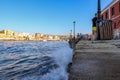 Interesting photo of wave hitting harbor with tourist waling and sitting.